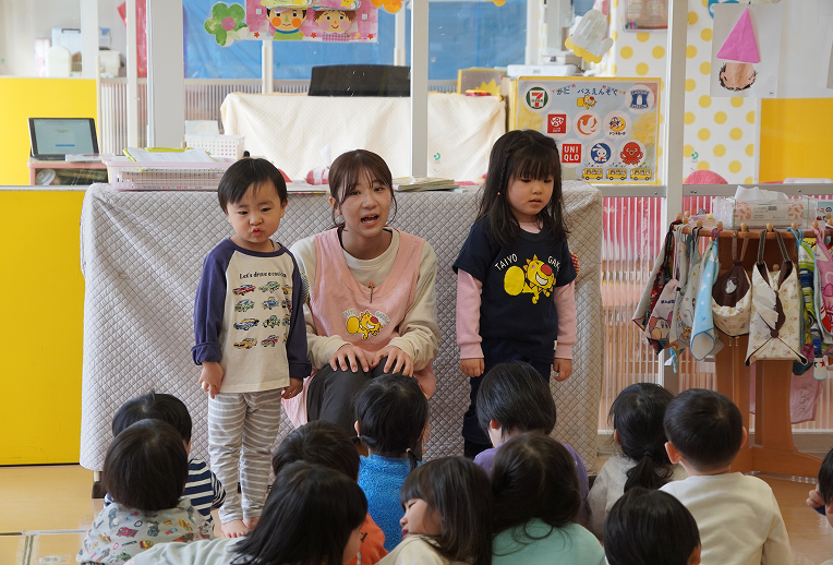 朝の会でみんなの前に立つ先生と二人の児童