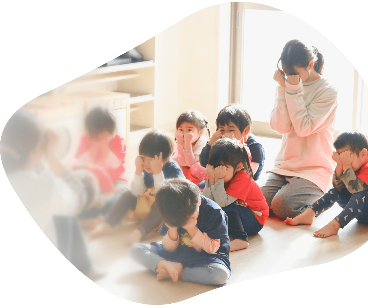先生と子どもたちが並んで座り、手で顔を隠している様子